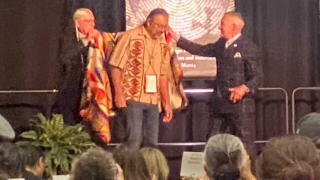 Cahuilla Artist Gerald Clark being wrapped in a blanket and receiving his medal.